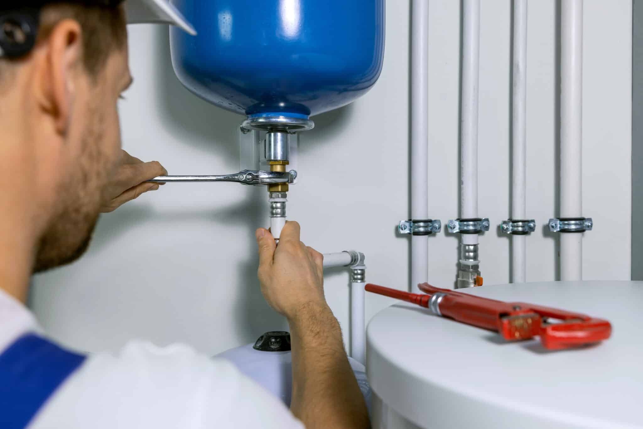 A plumber is using tools to fix a water heater.