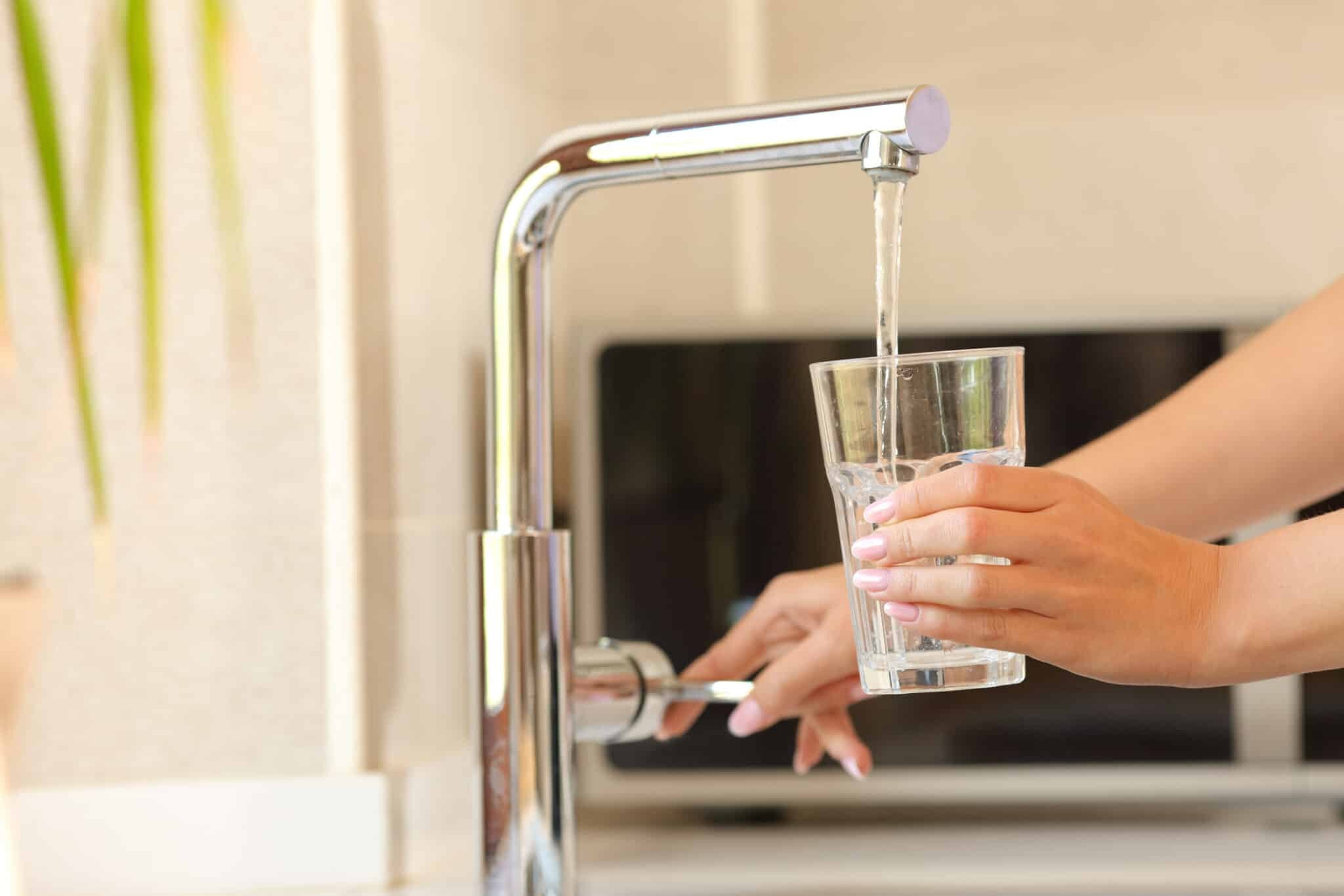 A glass is filling with water from a shiny, modern faucet.